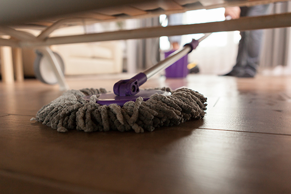 a maid is cleaning floor under the bed with mop